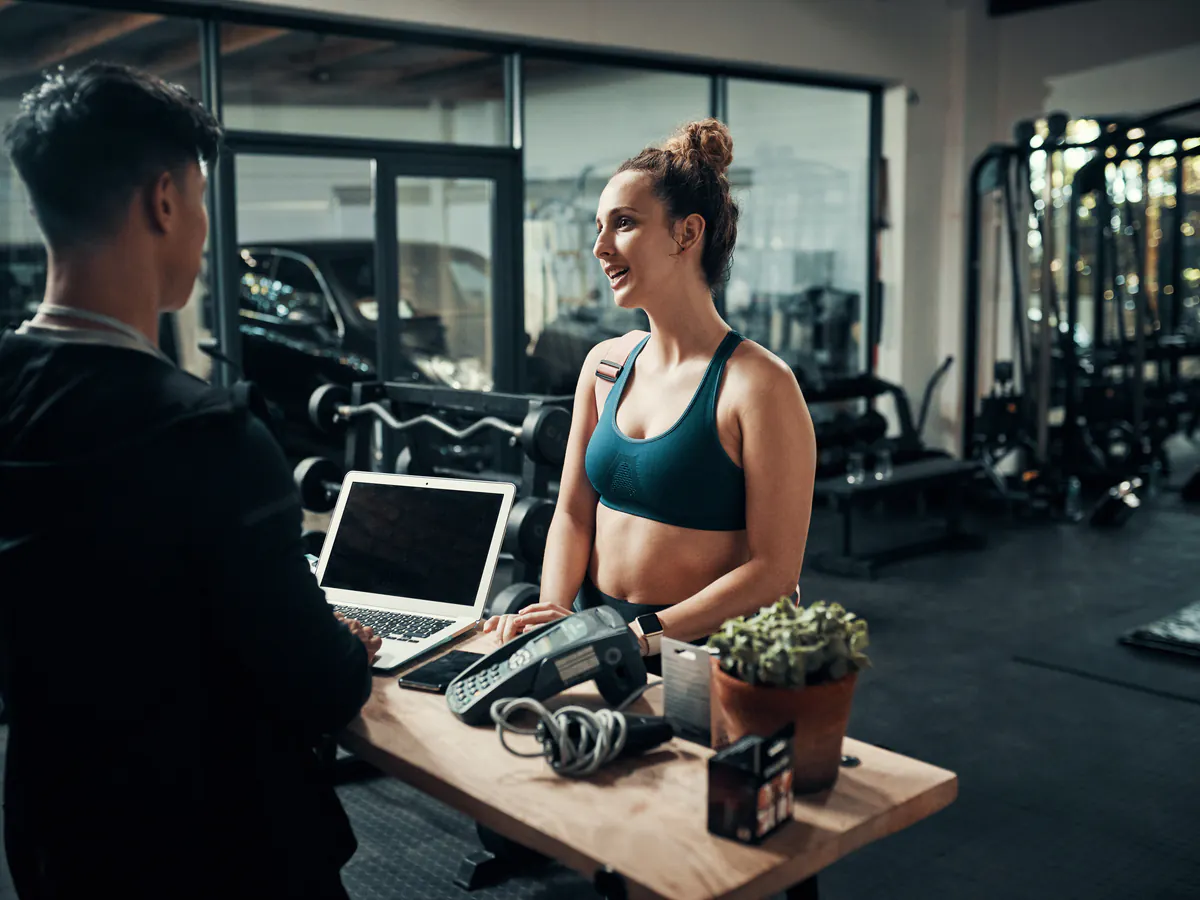 Recepción de gimnasio atiende a una nueva miembro como parte de la infraestructura digital para bienestar y fitness.