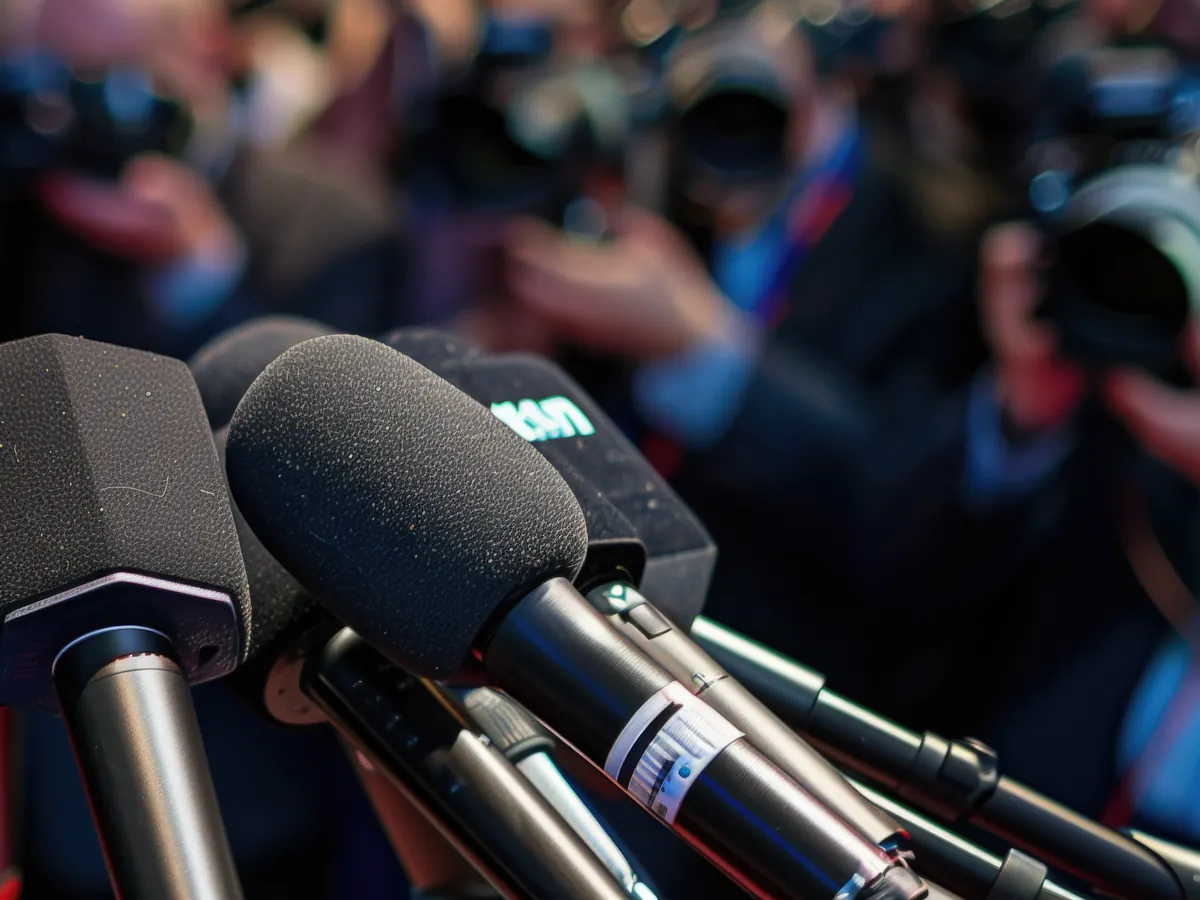 Micrófonos ante fotógrafos en una conferencia de prensa sobre representación pública de una marca.